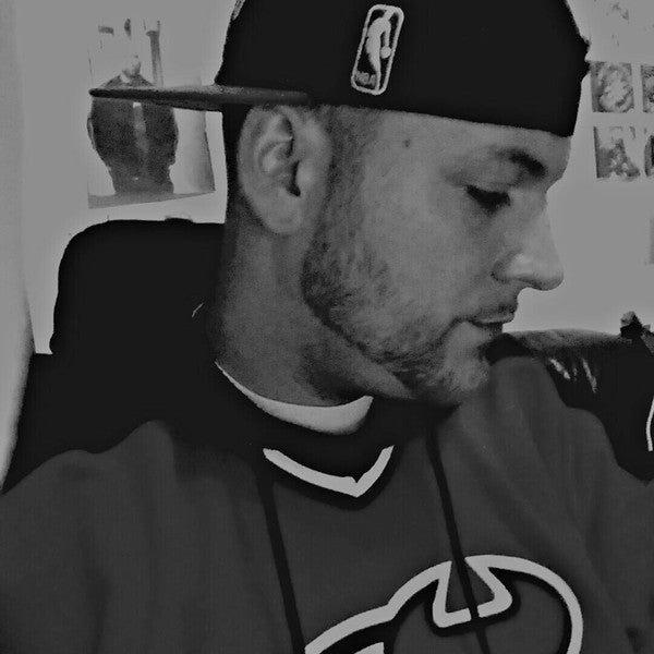 Black and white portrait of DJ Obsolete wearing a basketball cap and jersey, looking down with a focused expression.