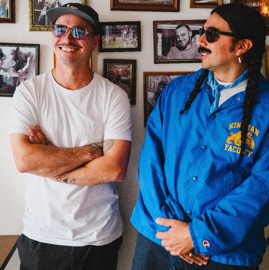 Two men standing in a room with framed pictures on the wall.