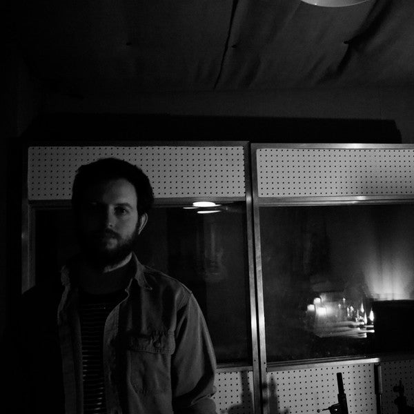 Robohands in a dimly lit recording studio, standing in front of a pegboard wall with a reflective surface. The moody black-and-white portrait emphasizes a contemplative atmosphere, capturing the essence of his jazz-influenced sound